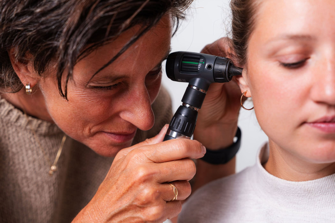 A GP examines a young patient’s ear with an otoscope.