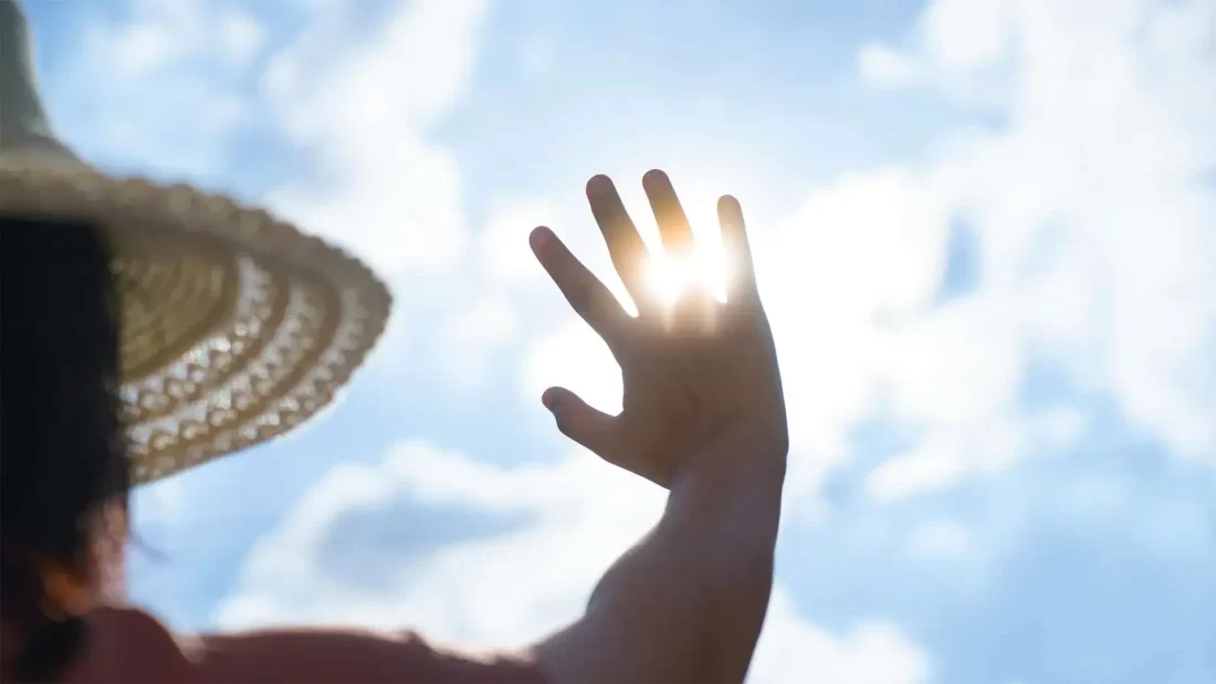 A person holds their hand up against the sun on a hot day.
