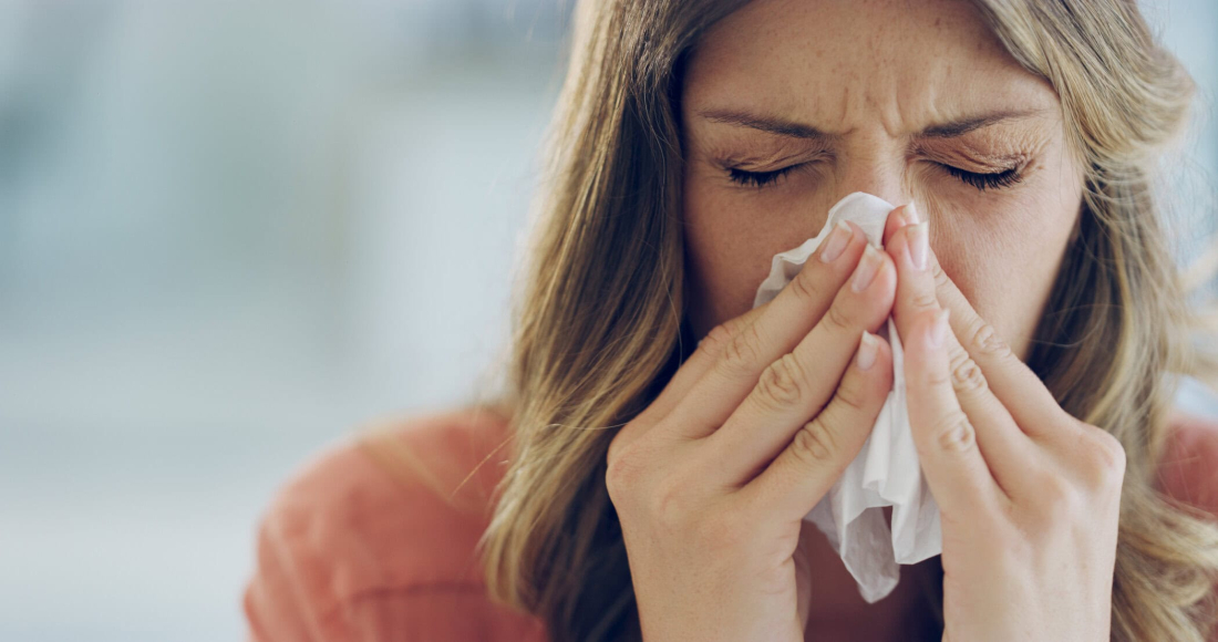 A shot of an attractive young woman who is feeling unwell, blowing her nose with a tissue at home