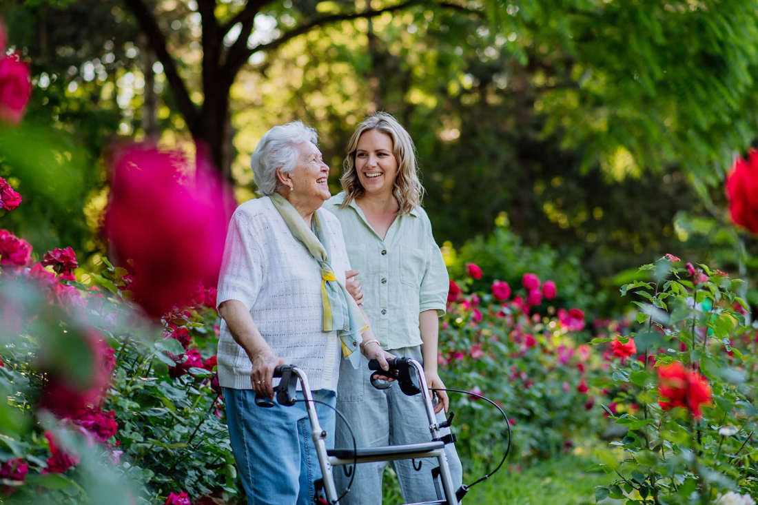 Vrouw met rollator en jonge vrouw in bloementuin genieten van de natuur.