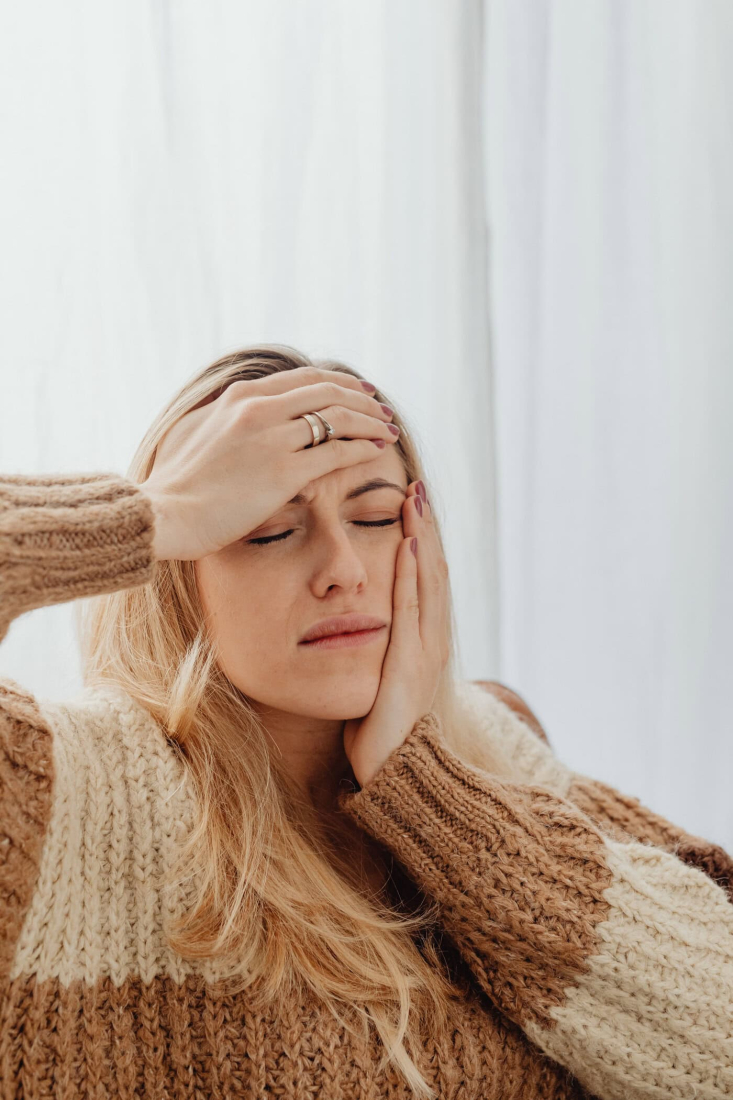 A woman with a headache is holding her head in a brightly lit room.
